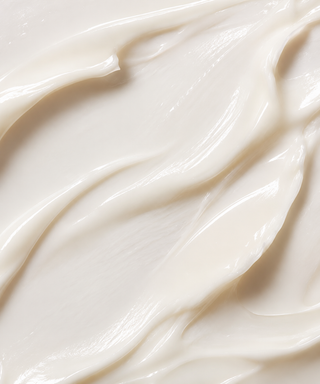 A close-up texture shot of a thick, creamy off-white Florettee cream with smooth, flowing swirls and soft highlights.