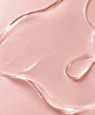 A close-up of a translucent, rose water spread across a matching light pink background.