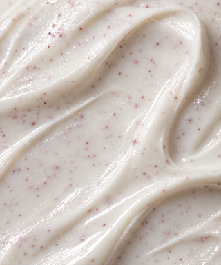 A close-up texture shot of a thick, creamy off-white Florettee cream with small pinkish-red specks throughout, swirled in smooth folds.